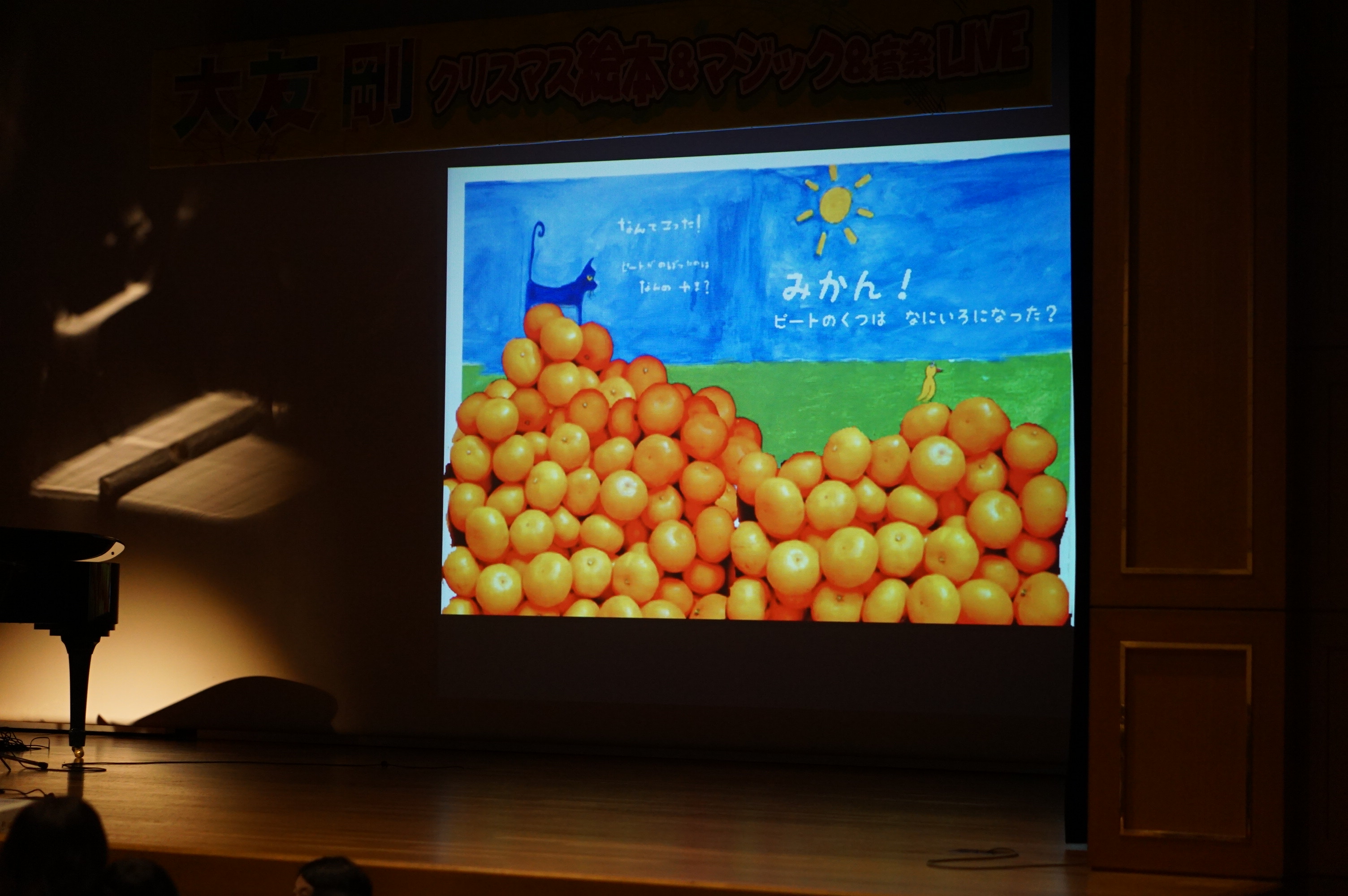 みかんとピートが描かれた絵が舞台上のスクリーンに映し出されている写真