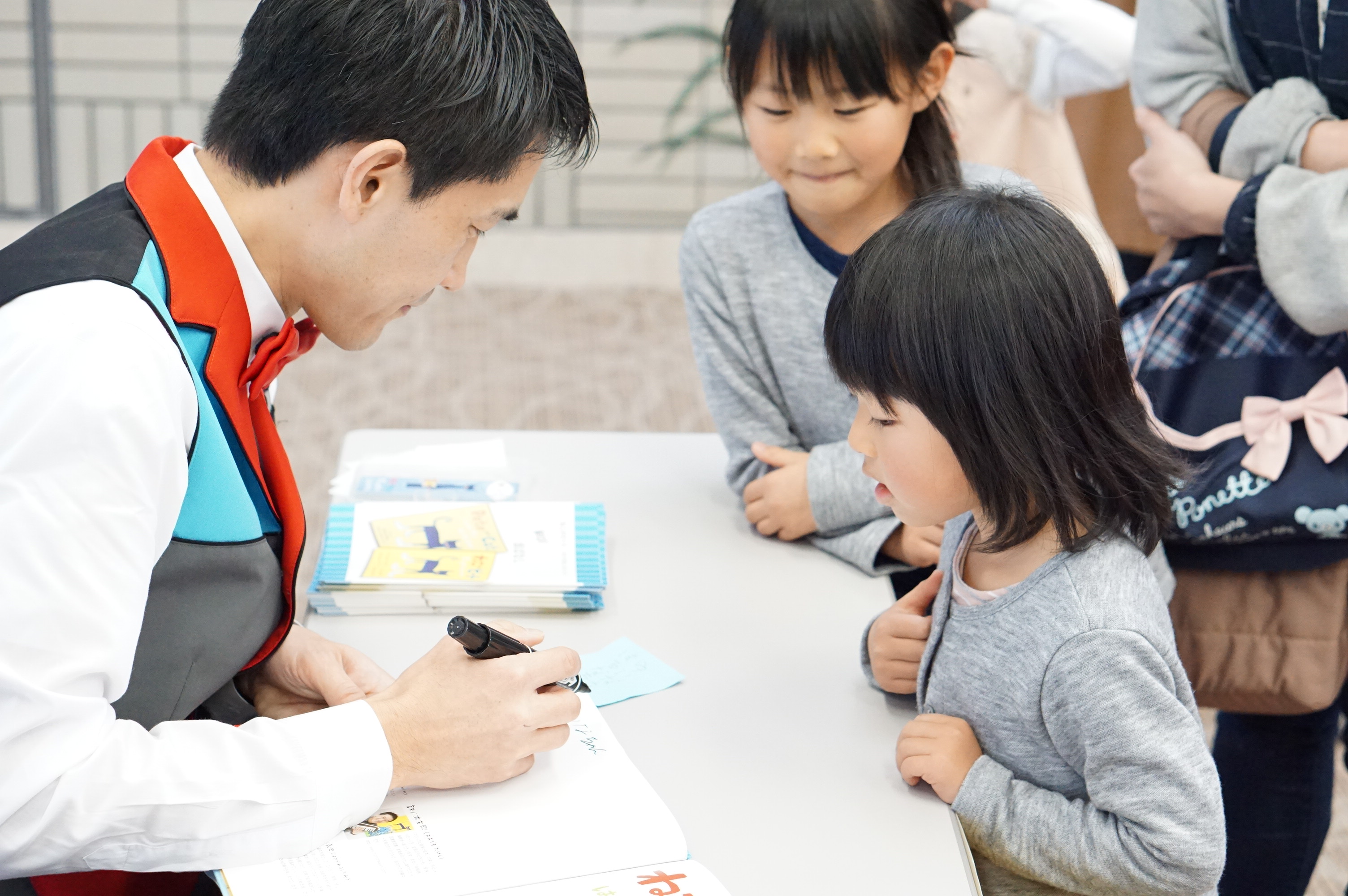 サインをする大友さんと、それを見守る子どもの写真