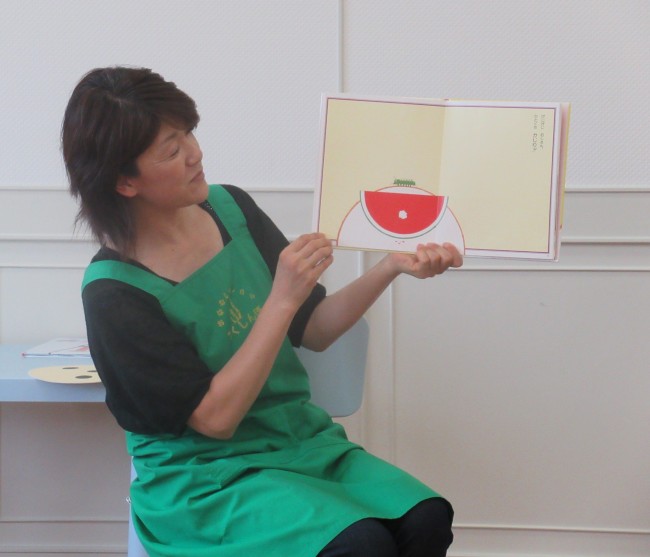 読み聞かせの様子で、スイカが描かれている絵本とスタッフの写真