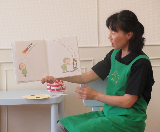 読み聞かせの様子で、子どもが描かれている絵本とスタッフの写真