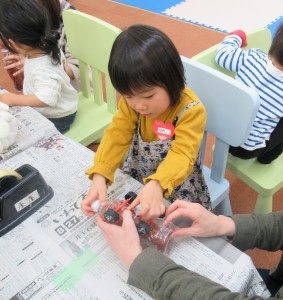 ペットボトルの裏にタイヤをつけようとする子どもの写真