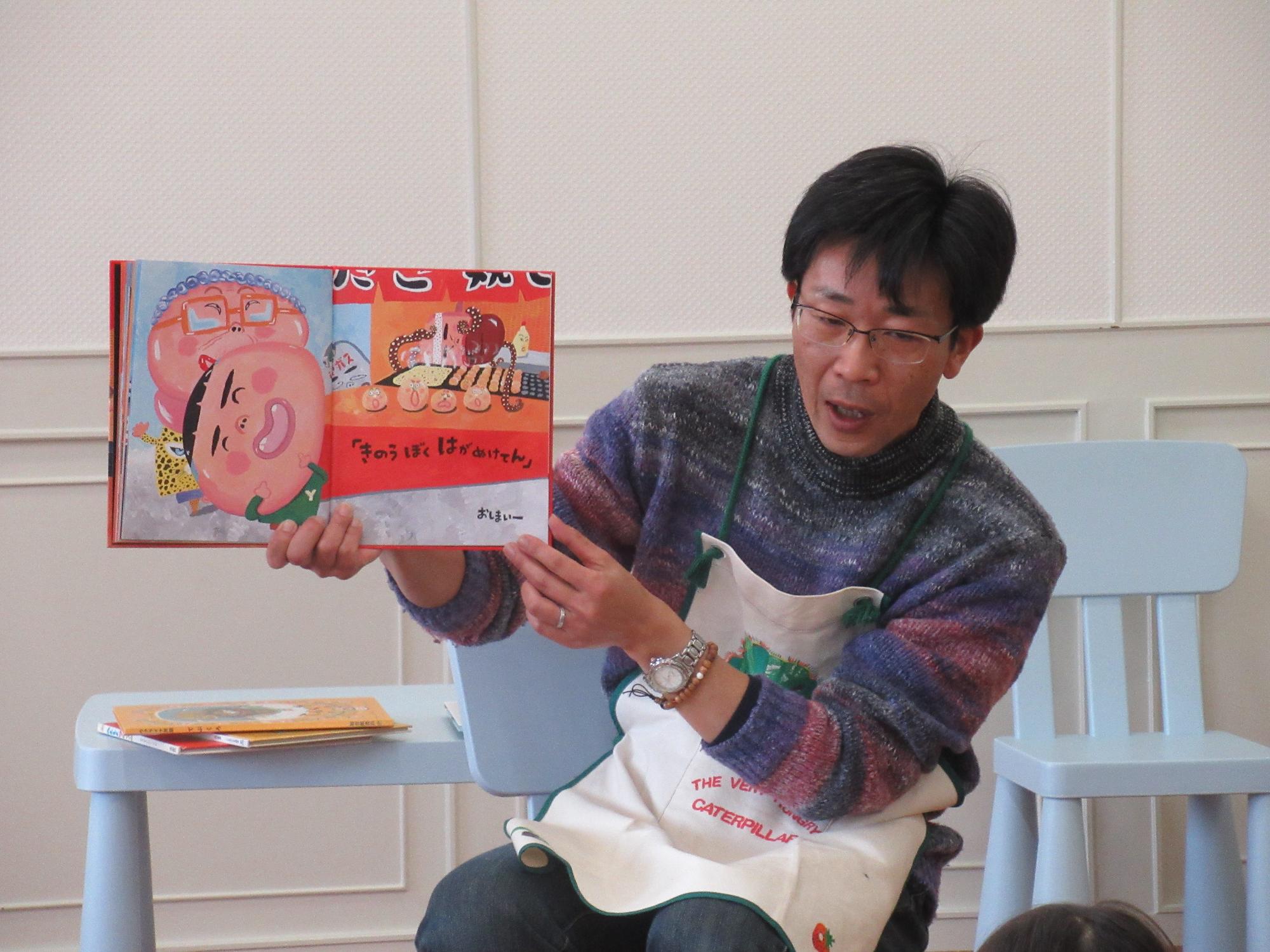 楽しそうな絵柄の絵本を見せながら読むスタッフの写真