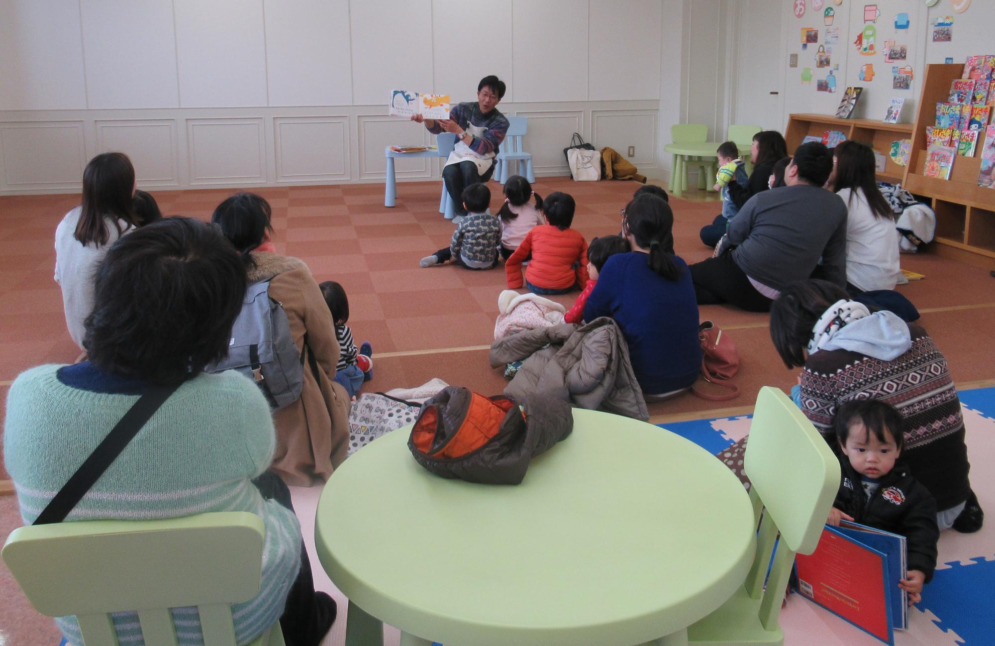 読み聞かせしているスタッフを聞き入る親子の写真