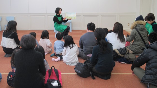 読み聞かせをしている女性と聞き入る参加者の親子の写真