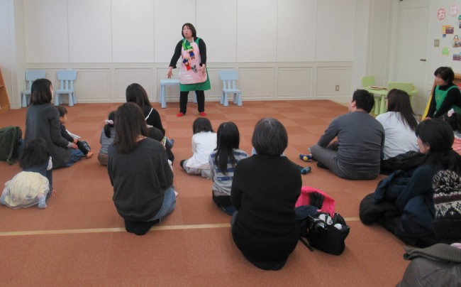 身振りを交えて読み聞かせる女性とそれを聞く参加者の親子の写真