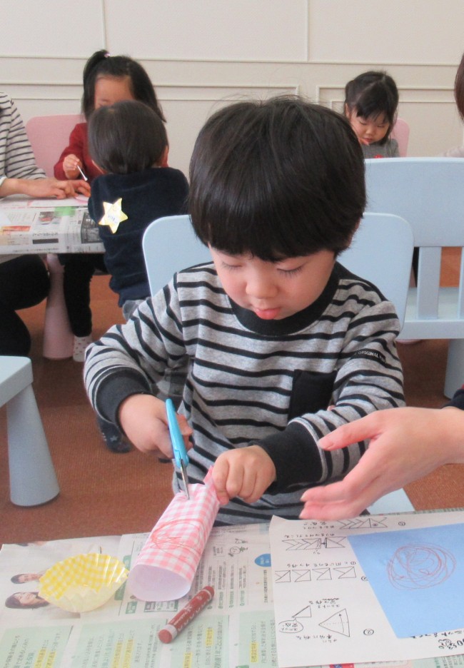 筒所にした折り紙をはさみで切る子供の写真