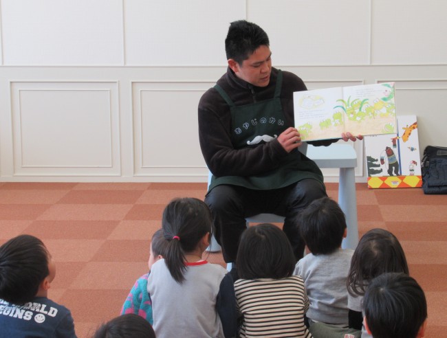 読み聞かせをするスタッフと聞き入る子どもたちの写真