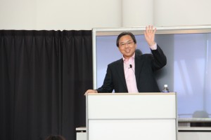 壇上で片手をあげる阿部恵さんの写真
