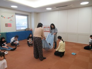 大きな布の両端を大人が持ち、ハンモック状になった中に赤ちゃんが寝ている写真