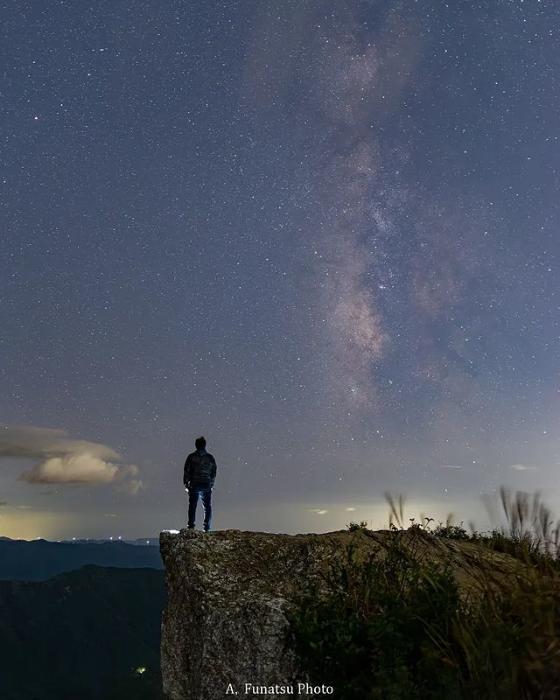 生石高原の夜空に天の川が流れ、男性が見上げている写真