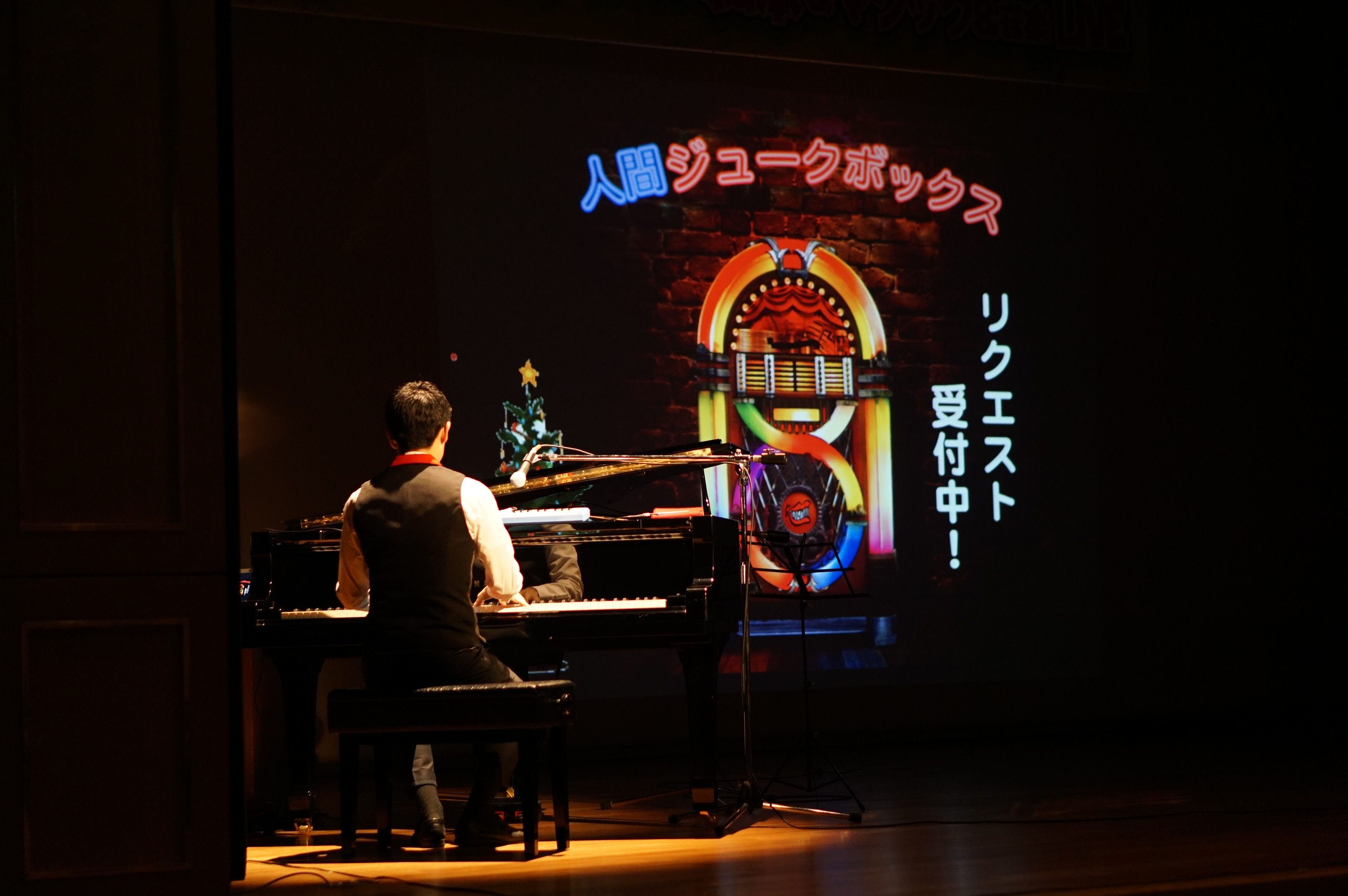 「人間ジュークボックス」とかかれた舞台装置の前でピアノを弾く大友さんの写真