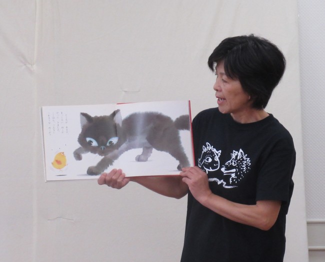 絵本の黒猫とひよこのページを見せながら読むスタッフの写真