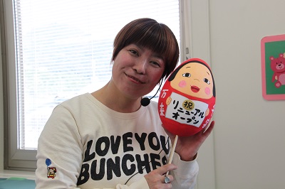 青山先生がリニューアルオープンと描かれただるまを持ってポーズを決めている写真