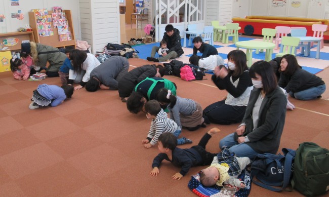 床にうずくまる体操をする参加者の親子の写真