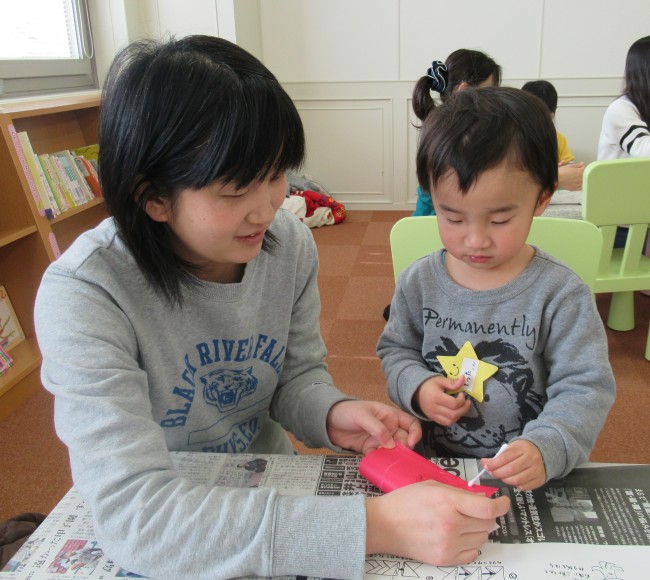 筒状にした折り紙にのりを塗っている子供の写真