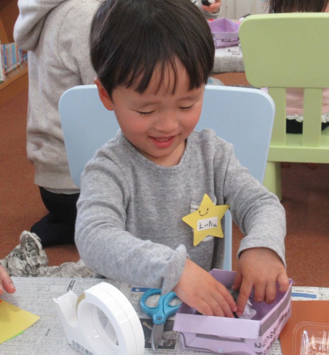 作った紙製のごはんを紙製のお弁当箱に入れる子どもの写真