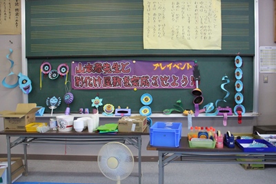 「山本孝先生とおばけ屋敷を完成させよう！」の横断幕と、お化けを作るためのパーツなどが置かれた写真