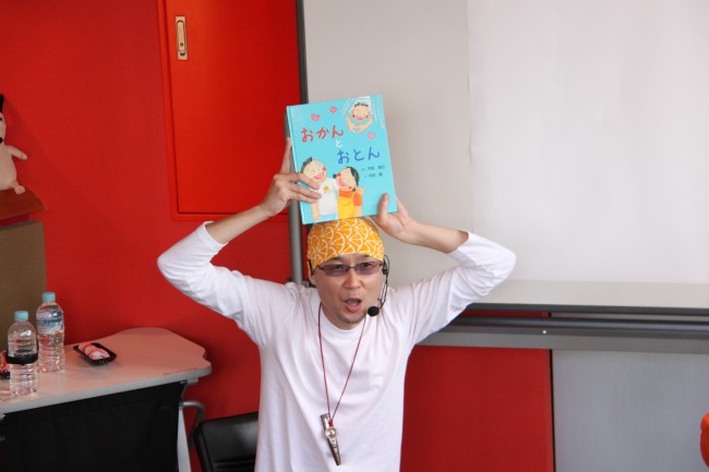 絵本「おかんとおとん」を頭に乗せている先生の写真